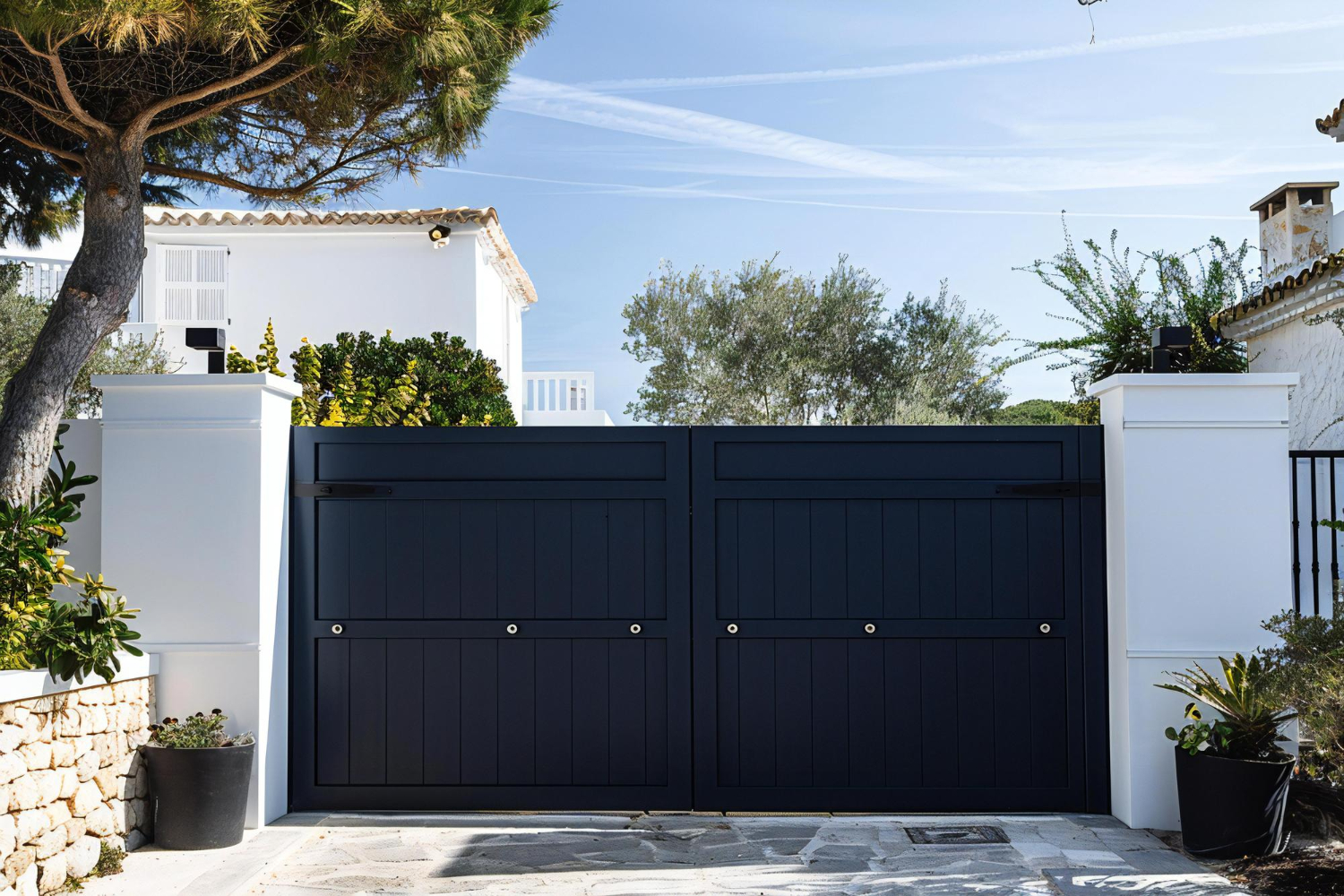 Un portail d'entrée coulissant noir avec mur blanc devant une maison